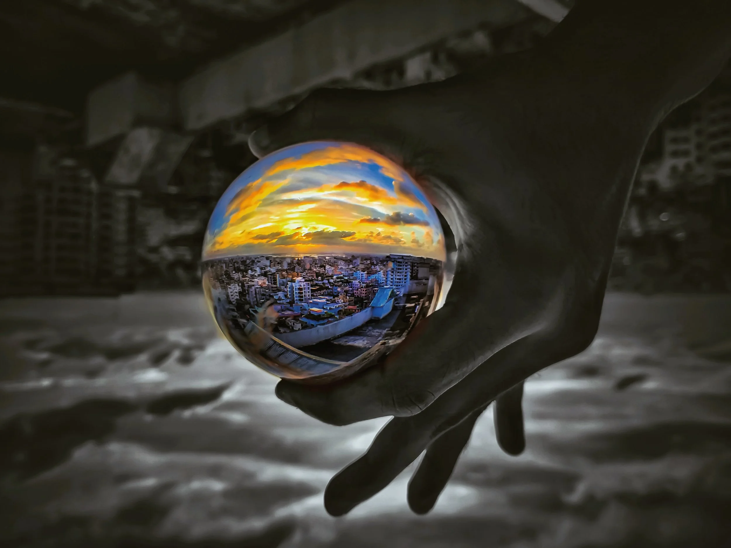 A hand holding a glass sphere reflecting a city skyline at sunset